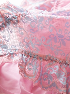 Close-up of pink lace fabric with blue floral embroidery and ruffle trim detail