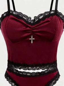 Dettaglio di lingerie in velluto bordeaux con pizzo nero e ciondolo a croce argento