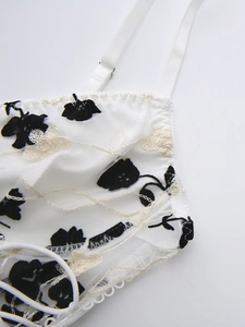 Close-up of white mesh lace camisole with black floral flocking and embroidery detail