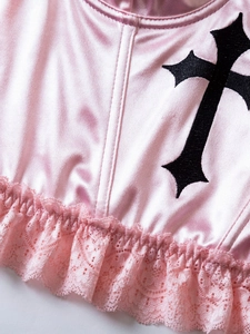 Close-up of pink satin top with black cross embroidery and delicate lace trim