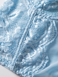 Macro detail of light blue floral lace and sheer mesh fabric with precise stitching