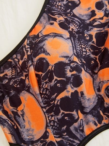 Detailaufnahme des orangefarbenen Stoffes mit Totenkopf-Druck und schwarzer Paspelierung