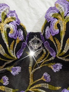 Detail of purple floral embroidery on black mesh with silver bat pendant ornament