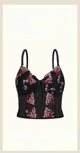 Close-up of red and white floral embroidery on black mesh corset top with bow detail