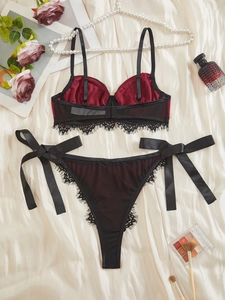 Dettaglio di lingerie in raso rosso con pizzo nero e fiocchi su seta color bianco crema