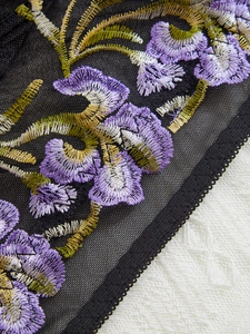 Macro detail of intricate purple floral embroidery on black mesh with lace trim