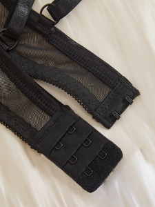 Dettaglio reggiseno in rete nera con chiusura a tre ganci e spalline in raso