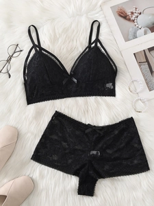 Flat lay view of a black lace lingerie set with bow details on a white faux fur background