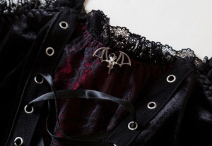 Detail of gothic black velvet corset with red lace and silver bat metal accessory