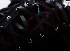 Macro detail of black velvet and red lace corset top with criss-cross ribbon lacing and eyelets