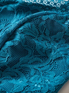 Close-up of deep teal lace fabric with delicate floral embroidery and mesh texture