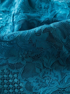 Close-up of deep teal lace fabric with intricate floral crochet and breathable mesh texture
