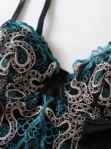Detailed close-up of intricate peacock blue floral embroidery on black lace bodysuit