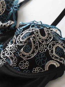 Gros plan d'un body en dentelle noire avec broderies florales bleues et détails satin