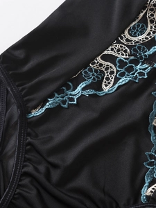Detail shot of black lace bodysuit featuring blue floral embroidery and pleated edges