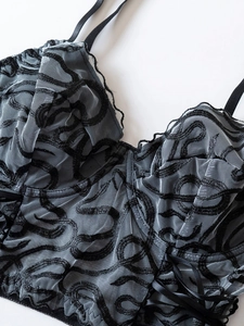 Détail de bralette en maille grise avec broderie noire, dentelle et nœud en satin