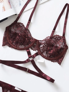 Dettaglio di reggiseno in pizzo bordeaux con cinghie harness e anelli d'argento