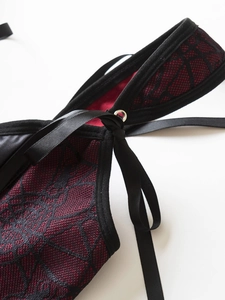 Detailed view of red lace fabric with black corset lacing and silver metal eyelets