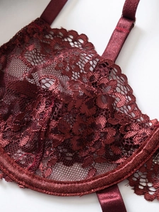 Dettaglio macro del reggiseno in pizzo bordeaux con motivi floreali e fibbie in metallo
