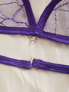 Macro shot of purple lace bra detail featuring a silver gothic bat pendant charm