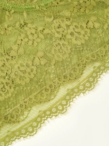 Detailed close-up of avocado green floral lace fabric with delicate eyelash fringe edges