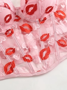 Detail of pink lace corset featuring red lip prints and heart embroidery with boning