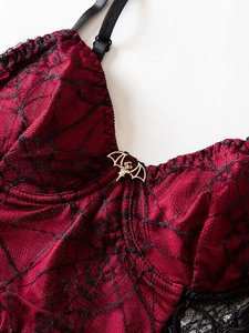 Detail of gothic dark red lace camisole featuring black spiderweb lace and bat pendant