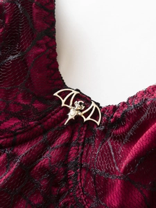 Close-up of burgundy satin with black lace and silver metal bat pendant on Gothic camisole