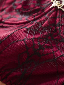 Macro detail of red Gothic camisole with black spiderweb lace and silver bat metal charm