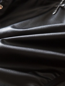 Detailansicht aus schwarzem PU-Leder mit Metallösen und einem Kreuzanhänger-Detail