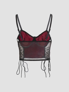 Detail of red satin corset top featuring black lace trim and intricate mesh paneling