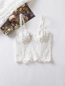 Close-up of white lace corset top featuring floral embroidery and pearl-beaded cups