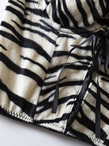 Detail of zebra print faux fur fabric with black satin lace-up ties and zigzag stitching