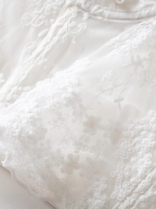 Close-up of white corset with intricate floral lace embroidery and elegant pearl button
