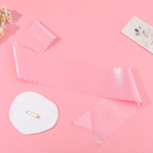Detail of light pink satin sash with scalloped edges and gold safety pin for DIY parties
