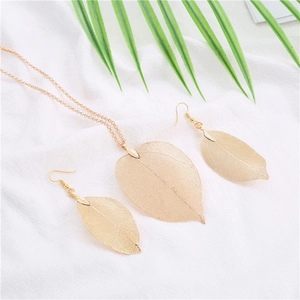 Detailed macro view of golden leaf vein necklace and earring set on white fabric