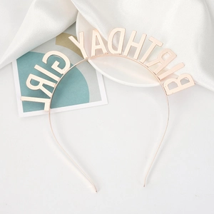 Detail of rose gold BIRTHDAY GIRL rhinestone headband on white silk and ceramic plate