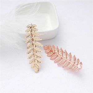 Detail of gold and rose gold leaf hair clips with white pearl accents on textured surface