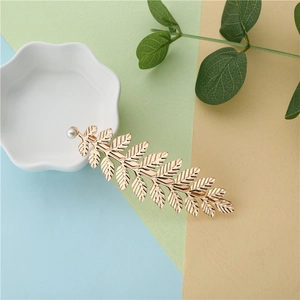 Detailed view of a gold leaf hair clip with a white pearl on a soft pastel background