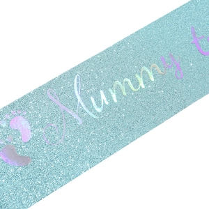 Nahaufnahme der hellblauen Glitzerschärpe Mommy to Be mit Laser-Schriftzug und Fußabdrücken