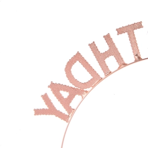 Detail of rose gold metal headband with textured YACHT letters for birthday party