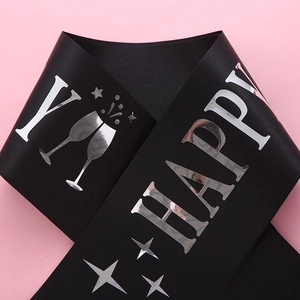 Detail of black satin birthday sash featuring silver foil Happy text and champagne icons