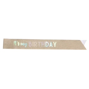 Dettaglio della fascia di compleanno glitterata con scritte olografiche su tessuto oro champagne