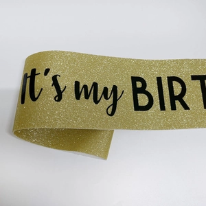Dettaglio della fascia di compleanno glitter oro con testo nero It's my BIRTHDAY