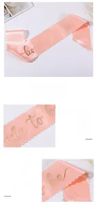 Close-up of pink satin bridal sash with scalloped edges and rose gold bride to be text