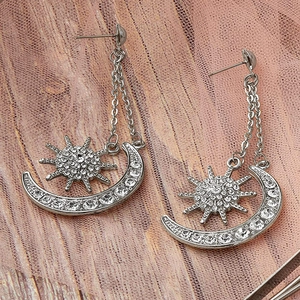 Macro shot of silver sun and crescent moon dangle earrings with white rhinestones