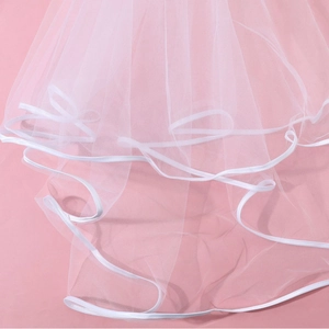 Elegant white double-layered bridal veil with satin edge and hair comb on pink background