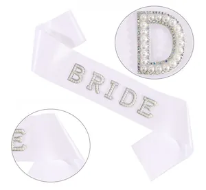 Close-up of white satin bridal sash featuring elegant pearl and rhinestone BRIDE lettering