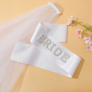 Detail of white bridal sash with pearl BRIDE lettering and matching wedding veil with comb