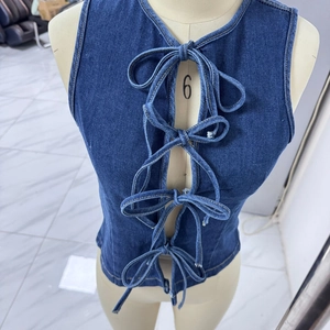 Detail of blue denim vest featuring four lace-up bow ties and contrast stitching